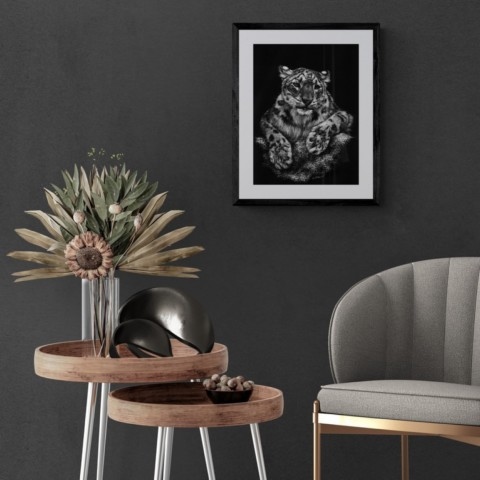 Framed scratchboard of a snow leopard displayed in a living‑room setting with a coffee table and an armchair – wildlife artist Laurence Saunois